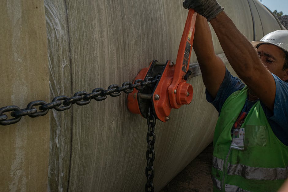 A construction worker using a chain and lever to secure a large pipe on site.